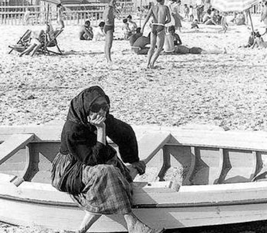 La Cagliari che non c’è più. Poetto, 1955: una signora anziana al mare si riposa su una barca vestita di tutto punto