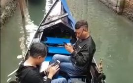 Turisti in gondola guardano lo smartphone