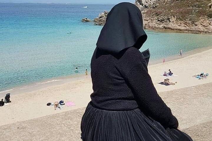La foto: una signora in costume sardo davanti alla spiaggia di Rena Bianca