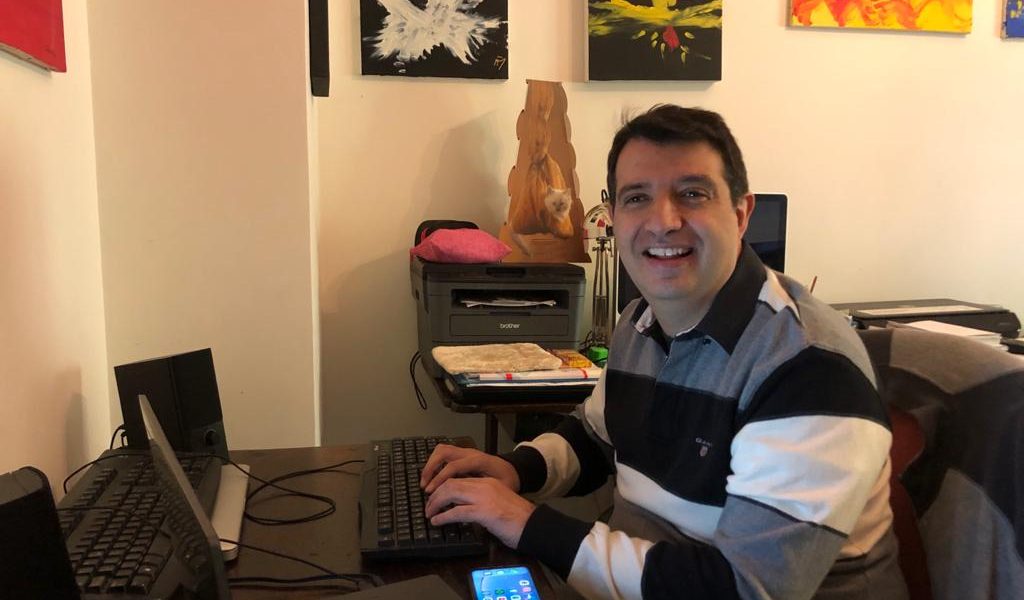 Andrea Ferrero, non vedente, circondato da tastiere dispositivi elettronici. Alle sua spalle alcuni dei suoi quadri.