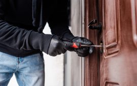 Cropped view of housebreaker in leather gloves breaking door lock with screwdriver