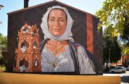 Una donna offre un dolce tipico sardo, fatto di mandorle e zucchero: dove si trova il nuovo murale di Mauro Patta?