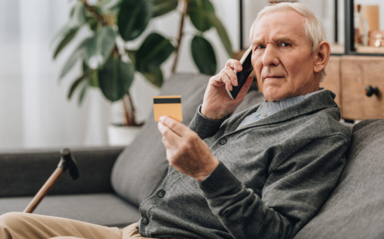 senior man talking on smartphone and holding credit card