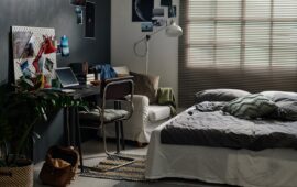 Double bed with grey cushions and blanket standing in front of desk with computer, photos and books in spacious bedroom of teenager