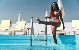 Enjoying summer day. Full length of playful young woman in red bikini splashing the water and smiling while standing in the swimming pool